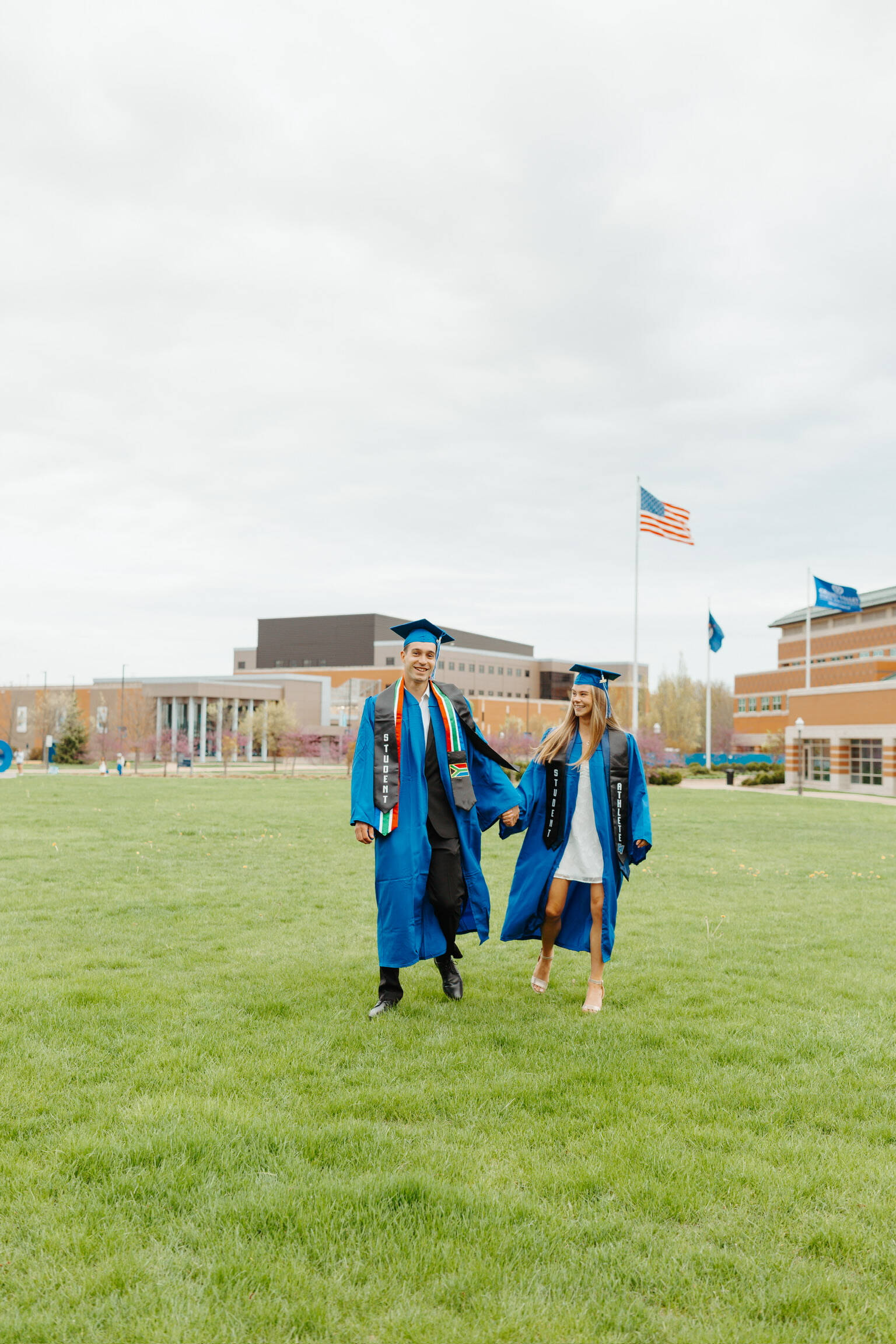 two students in GVSU regalia holding hands on GVSU campus